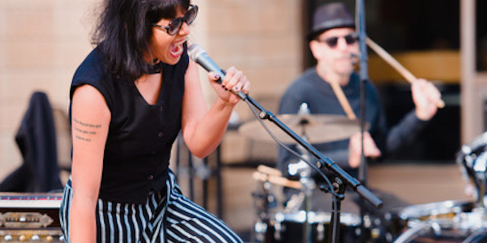 Shilpa Ray singing and standing on her red nord keyboard.
